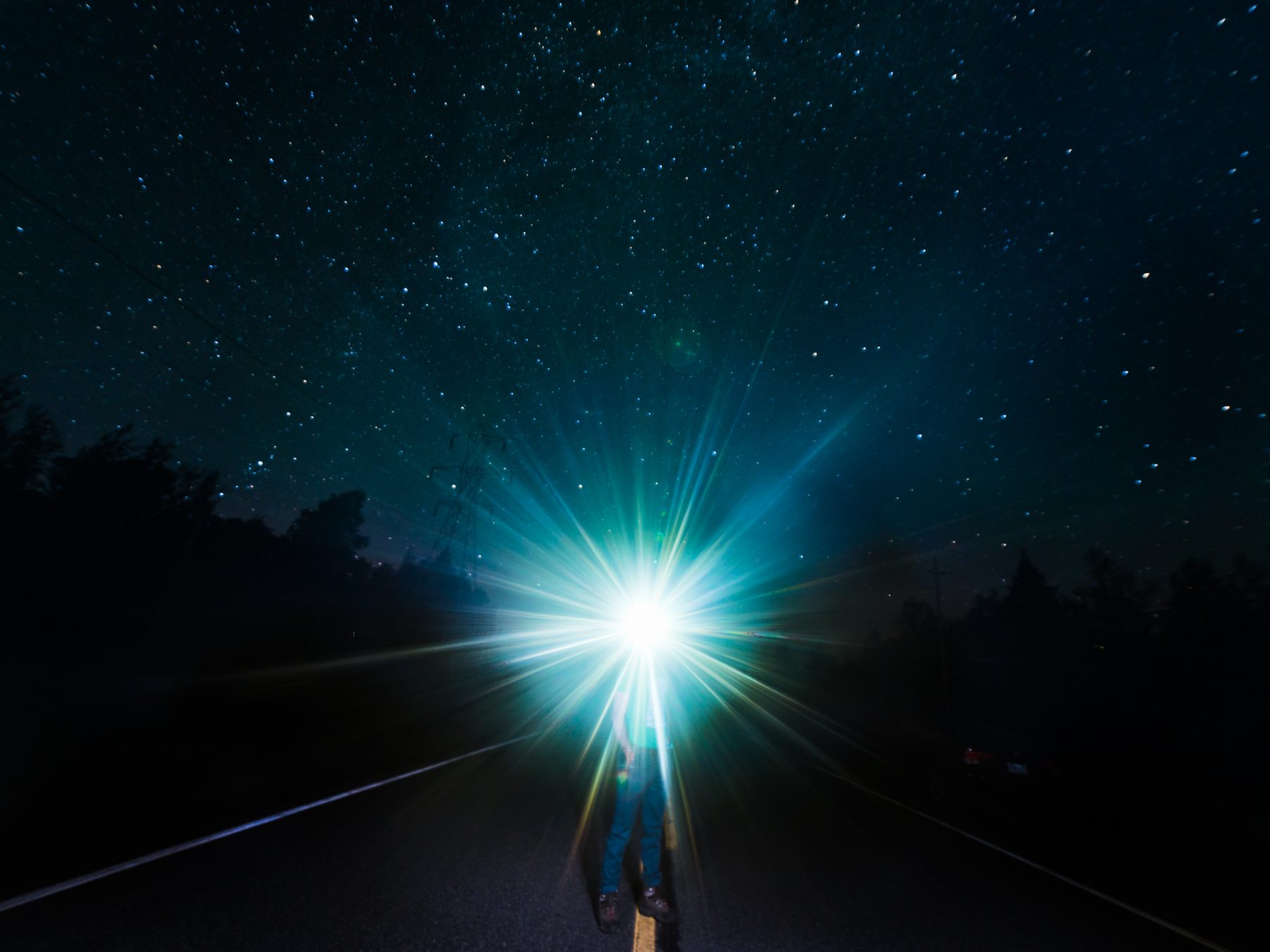 A headlamp starburst on a dark road under the stars